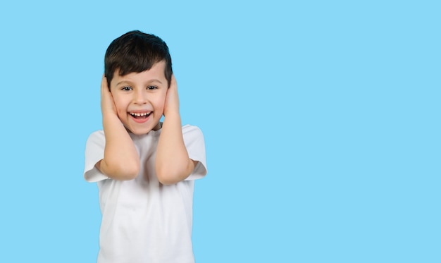 Un enfant dans un T-shirt blanc se couvre les oreilles avec ses mains et rit