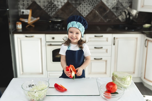 Enfant dans un tablier et une toque dans la cuisine prépare une salade