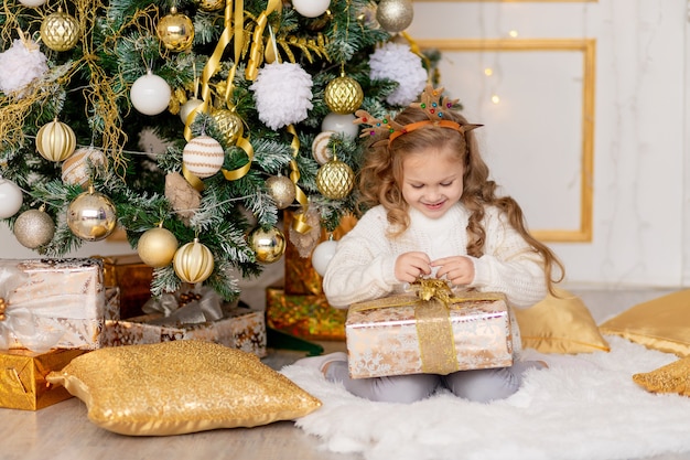 Un enfant déballe un cadeau du Nouvel An près d'un arbre de Noël avec un décor d'or à la maison