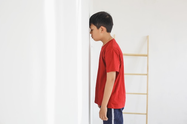 Enfant debout devant le mur parce qu'il a été puni par les parents, l'enfant se sent triste