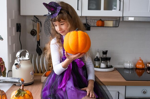 Un enfant décore la cuisine de la maison pour Halloween Une fille en costume de sorcière joue avec le décor pour les vacances chauves-souris jack lanterne citrouilles Confort d'automne dans la maison Scandistyle cuisine loft