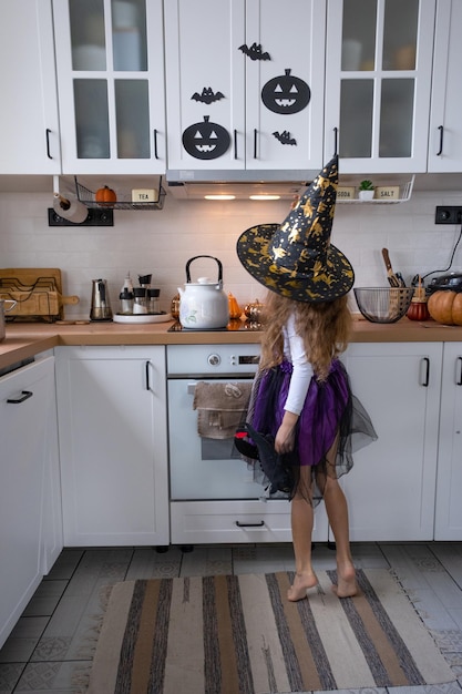 Un enfant décore la cuisine de la maison pour Halloween Une fille en costume de sorcière joue avec le décor pour les vacances chauves-souris jack lanterne citrouilles Confort d'automne dans la maison Scandistyle cuisine loft