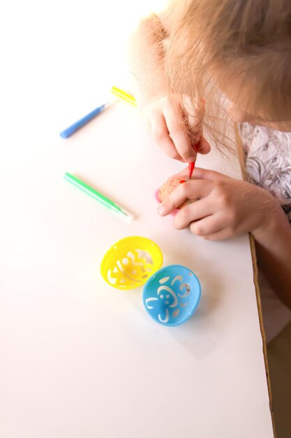 L'enfant décore les oeufs de Pâques avec des marqueurs de couleur et des gabarits en plastique