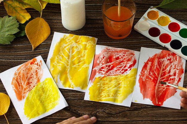 L'enfant découpe des feuilles d'automne avec une bougie et des aquarelles sur fond de bois