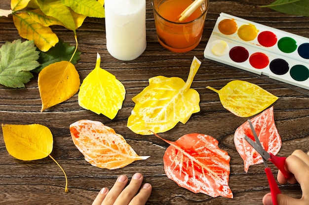 L'enfant découpe des feuilles d'automne avec une bougie et des aquarelles Projet d'art pour enfants