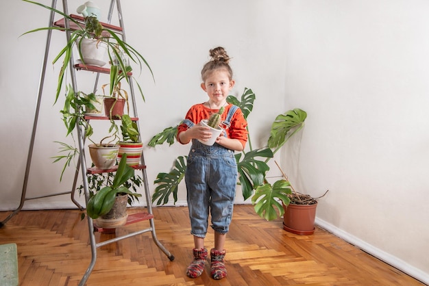 Enfant en denim tenant un pot de cactus sur le fondxAplantes d'intérieurxDans la serre Petite fille s'occupe des plantes vertes dans la chambre Jardinage à domicile école à la maison amour des plantes et des soins