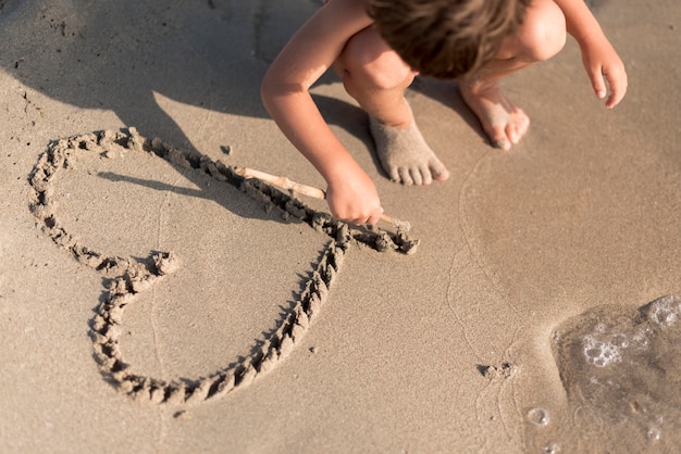 Enfant dessinant un coeur dans le sable