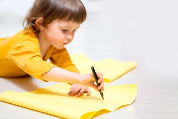 L'enfant dessine sur du papier avec des feutres allongés sur le sol