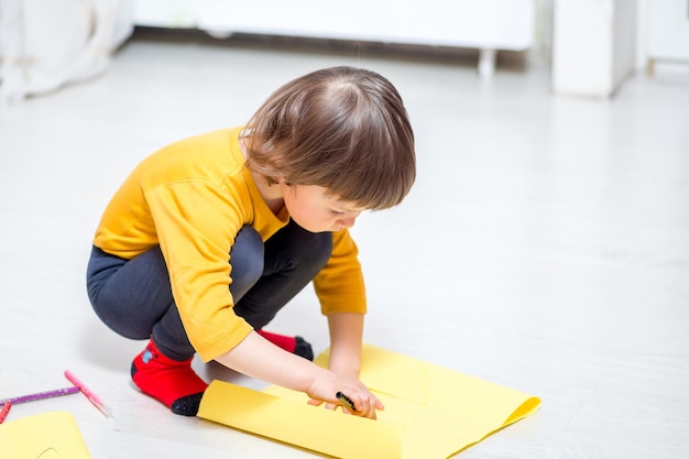 L'enfant dessine sur du papier avec des feutres allongés sur le sol