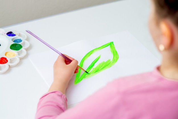 L'enfant dessine une feuille verte à l'aquarelle sur du papier blanc. Jour de la terre et concept de protection de l'environnement.