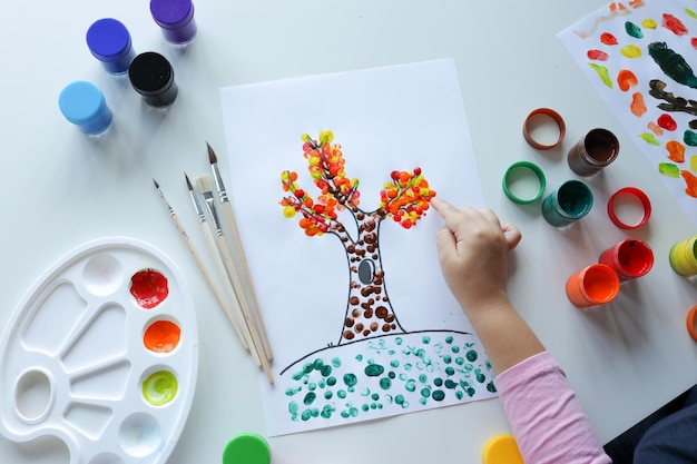 Un enfant dessine des feuilles sur un arbre Idées pour dessiner avec des peintures au doigt Peinture au doigt pour les enfants sur fond blanc Petite fille peignant au doigt la couleur de la peinture à la main Concept de développement des enfants