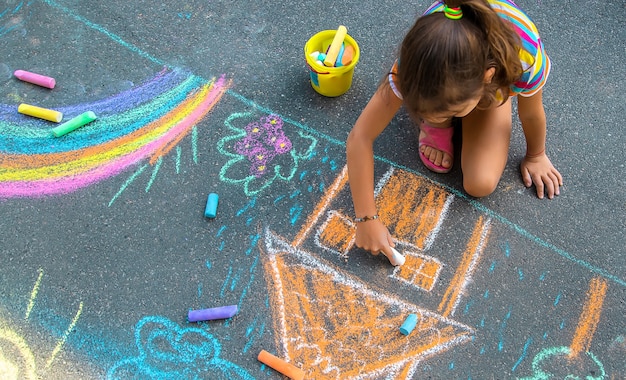 L'enfant dessine une maison et un arc-en-ciel sur l'asphalte avec de la craie