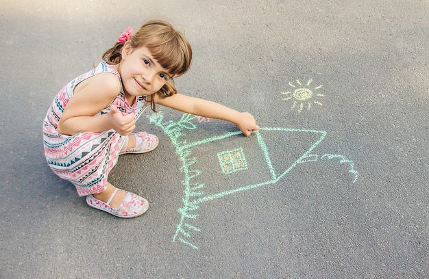 L&#39;enfant dessine la maison à la craie sur l&#39;asphalte. Mise au point sélective.