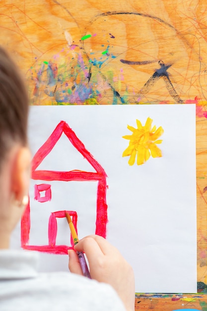 L'enfant dessine la maison.