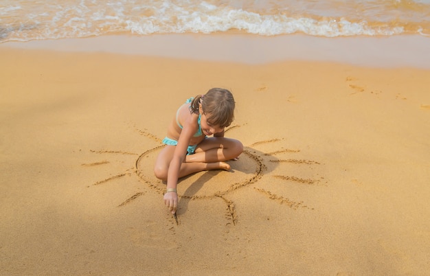 Un enfant dessine un soleil sur la plage.