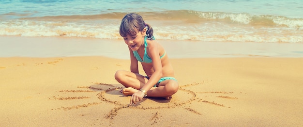 Un enfant dessine un soleil sur la plage