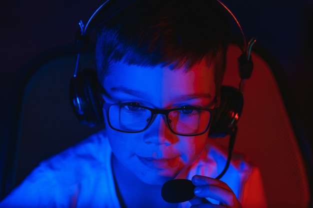 Un enfant diffuse un jeu informatique en ligne, un garçon diffuse dans des écouteurs sur fond d'éclairage RVB