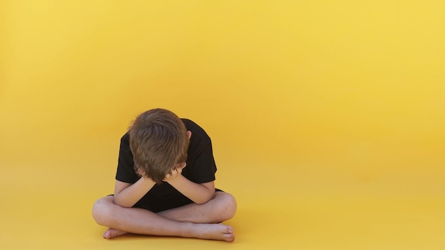 Un enfant dont la dépression est assis sur le sol de couleur