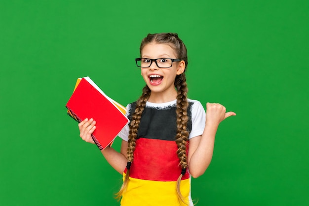 Un enfant avec un drapeau allemand pointe vers votre publicité et tient un carnet Une petite fille avec des lunettes sur un fond vert isolé
