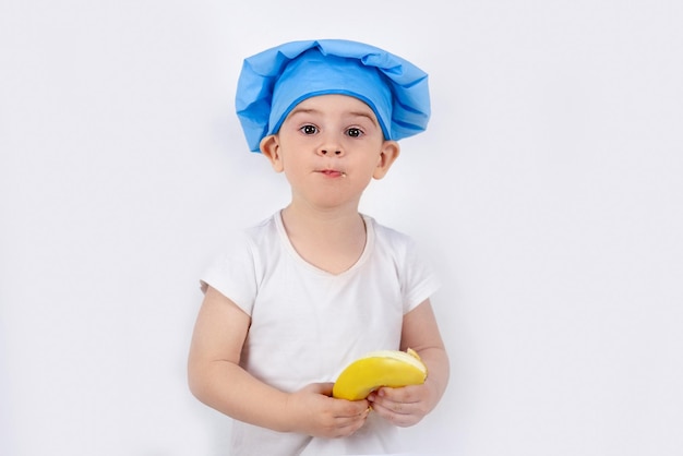 L'enfant drôle dans un chapeau de chefs mange une banane