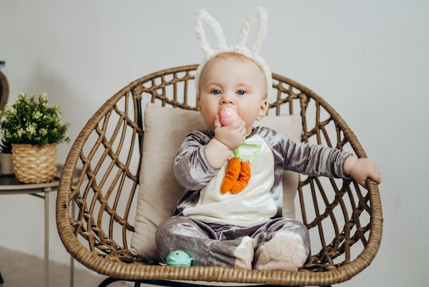 Un enfant drôle dans un costume de lapin est assis dans une chaise en osier Célébration de Pâques lapin de Pâques