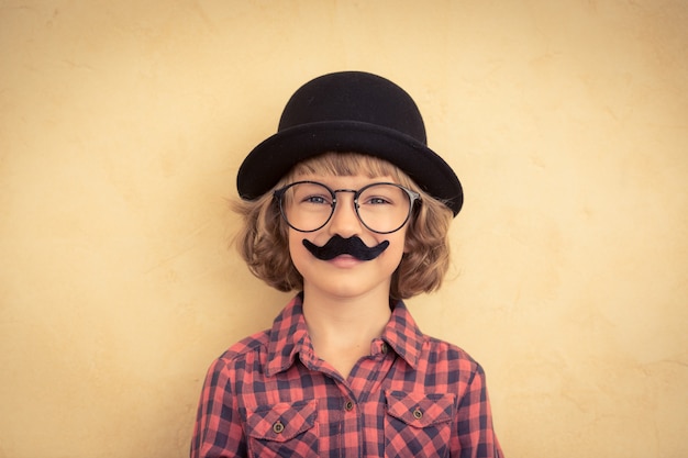 Enfant drôle avec une fausse moustache. Heureux enfant jouant à la maison