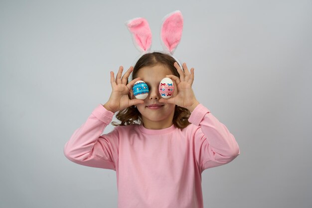 Une enfant drôle et heureuse avec des œufs de Pâques et des oreilles de lapin.