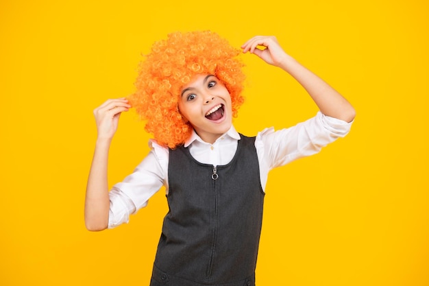 Enfant drôle avec une perruque de cheveux bouclés Mignonne petite fille avec des cheveux de fantaisie Enfant portant une perruque de cheveux de clown rousse brillante Visage excité émotions joyeuses d'une adolescente