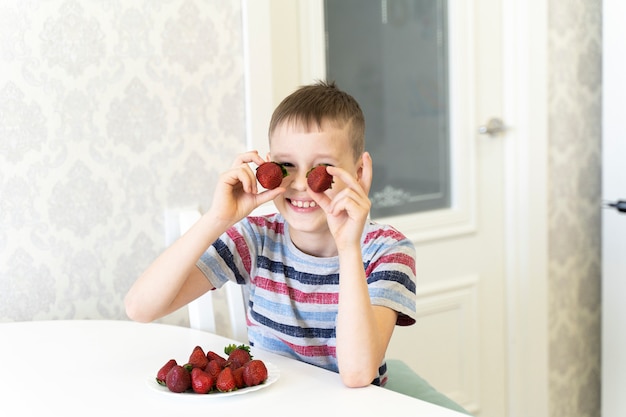 Un enfant drôle rit et met des fraises à la place des yeux