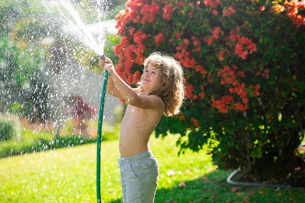 Un enfant drôle s'amuse et sourit heureux sur la nature arrière-cour arrosant les plantes dans le jardin à la maison sur la somme