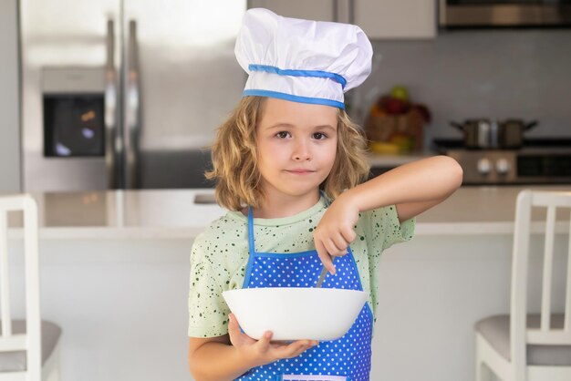 Un enfant drôle se tient à la table de la cuisine s'amuse à faire de la boulangerie en préparant des aliments à la maison