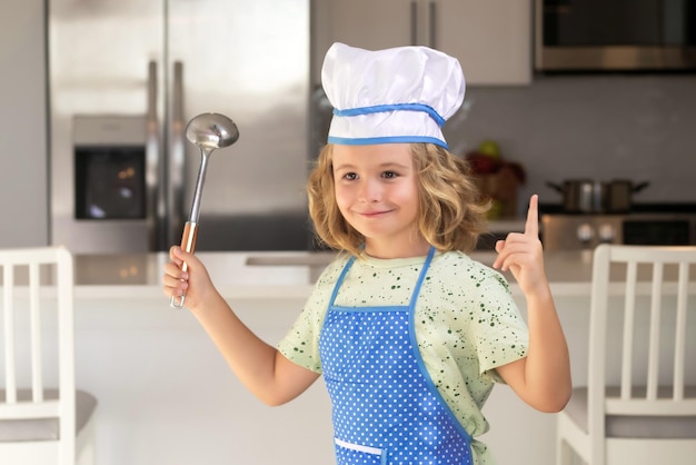 Un enfant drôle se tient à la table de la cuisine s'amuse à faire de la boulangerie en préparant des aliments à la maison