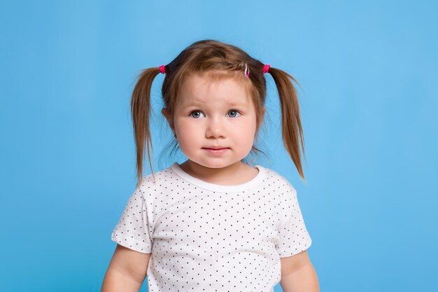 Enfant drôle en T-shirt blanc sur fond bleu. Petite jolie fille. Copiez l'espace pour le texte. Vente, vacances, concept de fête d'anniversaire.