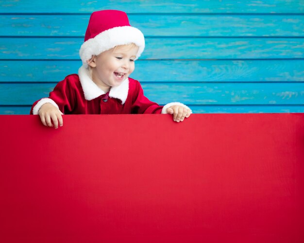 Enfant drôle tenant une bannière en carton vierge. Enfant jouant à la maison. Concept de vacances de Noël. Espace de copie.