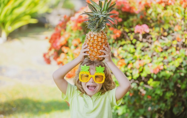 Enfant drôle tient un ananas sur sa tête sur un fond de nature d'été Ananas garçon et ananas en vacances d'été