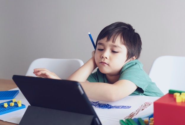 Enfant de l'école dans l'auto-isolement à l'aide de tablette pour les devoirs, enfant visage triste couché tête baissée regardant au fond de la pensée, éducation en ligne à distance