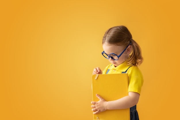 Enfant de l'école dans des verres fond jaune isolé tenir le livre scolaire Retour à l'école Éducation