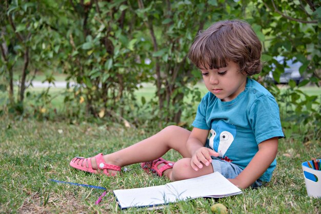 Enfant de l'école primaire allongé sur l'herbe à faire ses devoirs