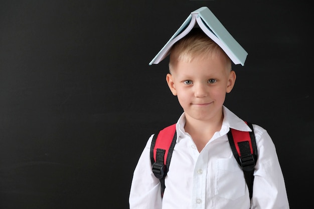 Enfant de l&#39;école primaire avec un livre sur sa tête au tableau