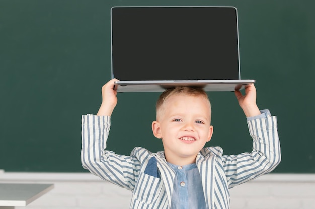 Enfant de l'école primaire tenant un ordinateur portable sur la tête en cours d'informatique