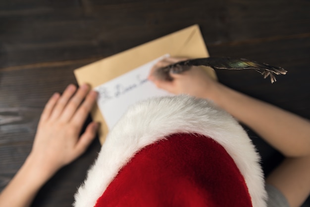 L'enfant écrit une lettre au père Noël dans le chapeau du père Noël. Vue de dessus. Noël