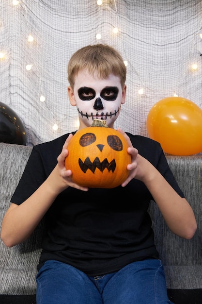 Enfant effrayant avec un maquillage en forme de squelette et avec une citrouille dans ses mains
