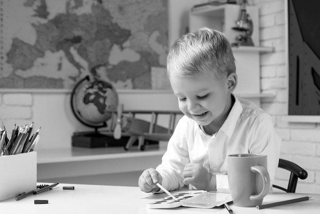 Enfant élève est assis à un bureau à l'intérieur mignon élève avec drôle de visage scolarisation travail enfants se prépare f