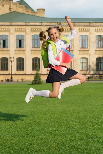 Enfant énergique en uniforme formel avec sac à dos de livres d'étude sauter dans la cour d'école heureux de célébrer la rentrée scolaire