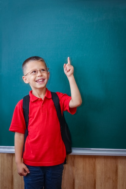 Un enfant enfant heureux debout au tableau avec un sac à dos d'école portant des lunettes