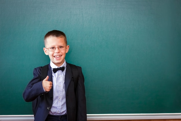 Un enfant enfant heureux debout au tableau avec un sac à dos d'école portant des lunettes