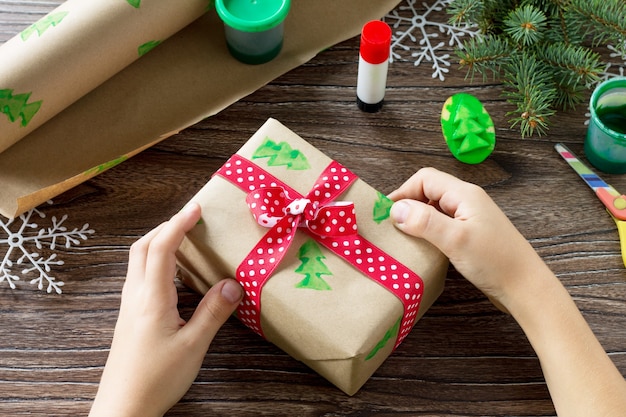 Un enfant enveloppe du papier avec une boîte de cadeaux de Noël et un bonhomme de neige de bonbons Projet d'art pour enfants