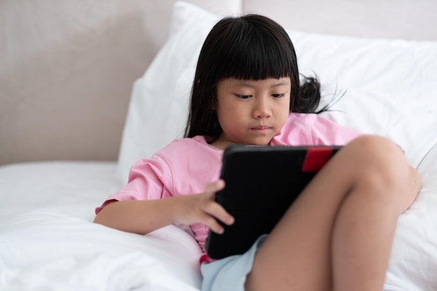 L'enfant est accro à la tablette petite fille jouant au smartphone enfant utilise le téléphone en regardant le dessin animé