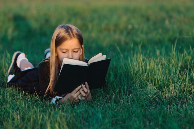 Un enfant est allongé sur l'herbe et lit un livre à la lumière du coucher du soleil.