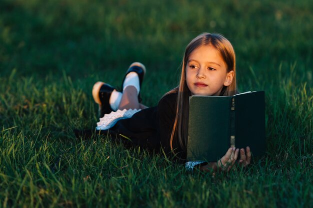 L'enfant est allongé sur l'herbe et tient un livre dans la lumière du coucher du soleil.